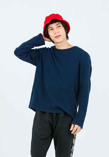 Full body studio shot Asian young handsome slim teenager fashion male model in street style outfit long sleeve shirt standing posing smiling holding hand adjusting red bucket hat on white background