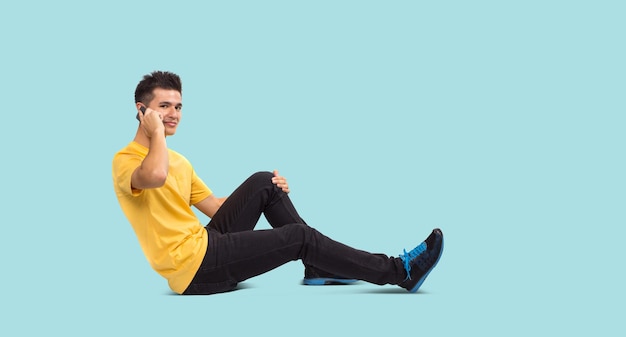 Full body Teenage boy portrait sitting using smart phone isolated on blue background