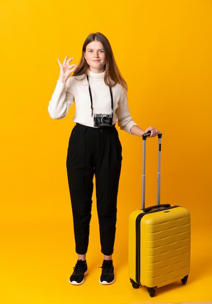 Full body of traveler teenager girl with suitcase showing an ok sign with fingers