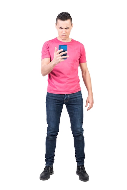 Corpo pieno di modello maschile insoddisfatto in abito casual che legge un messaggio di testo negativo sul cellulare su sfondo bianco