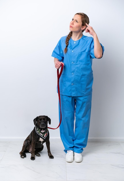 Full body veterinarian woman with a dog isolated on white background having doubts and with confuse face expression