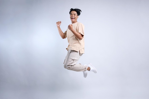 Full body view of young Asian man in casual clothes jump high do winner gesture and clench fist