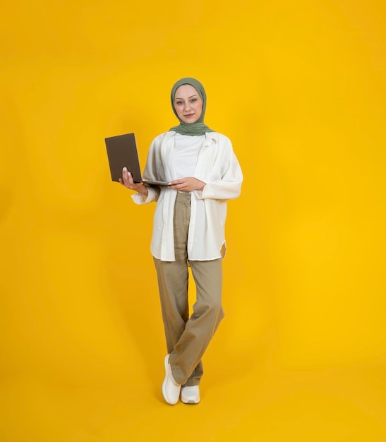 Full body view young caucasian muslim woman in hijab holding laptop working notebook pc computer