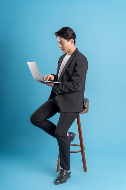 Full body young business man wearing a vest using laptop and posing on a blue background