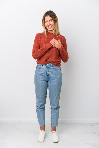 Full body young caucasian woman has friendly expression, pressing palm to chest.