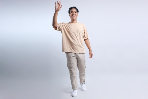 Full body of young smiling Asian man wear casual tshirt walking and waving hand warmth greeting