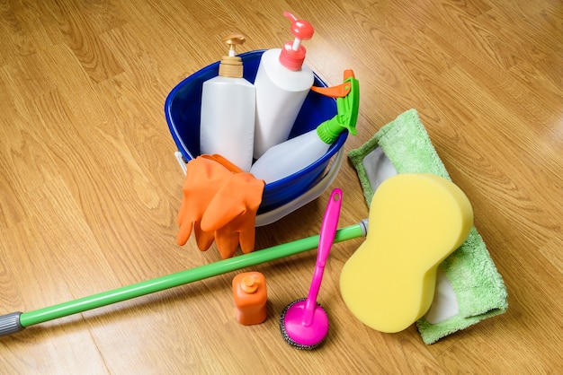 full box of cleaning supplies, mop and gloves on wooden background