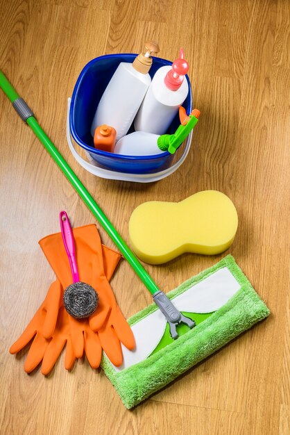 full box of cleaning supplies, mop and gloves on wooden floor background