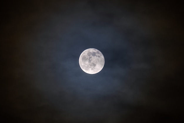 Full bright moon with illuminated clouds in front of it.