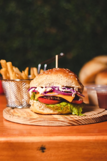 Full burger with fries in the background on top of a wooden table