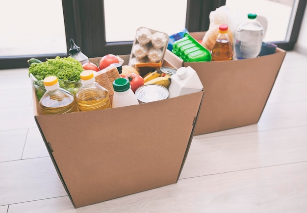 La scatola ecologica in cartone piena con i prodotti del negozio di alimentari sul pavimento di casa vicino alla porta