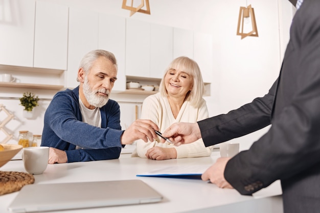 Full of determination. Decisive cheerful aged couple sitting at home and having conversation with social security advisor while signing the agreement