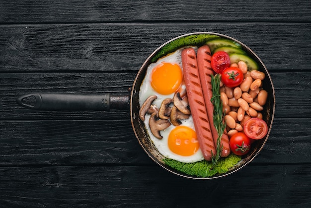 full english breakfast with fried eggs sausages beans toasts and coffee on copy space background on a black wooden background