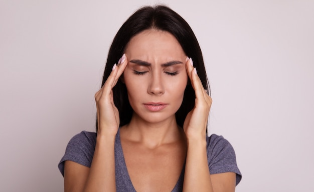 Full-face portrait of a girl, who is facing the camera with her eyes closed and her fingers touching temples as a sign of stress or headache