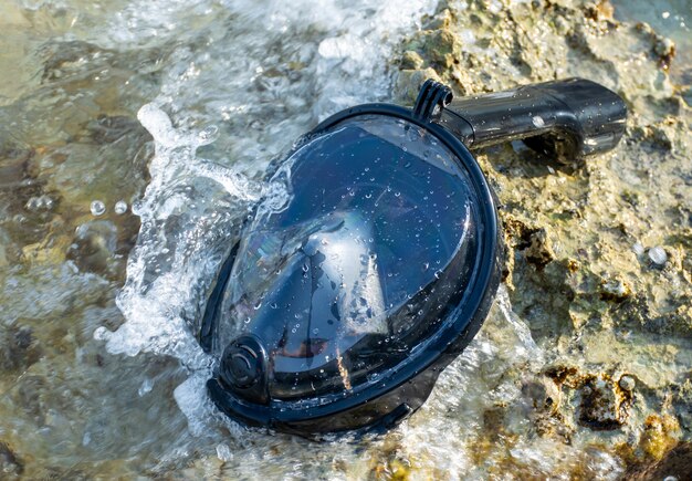 Full face snorkeling mask lies on the seashore washed by the waves