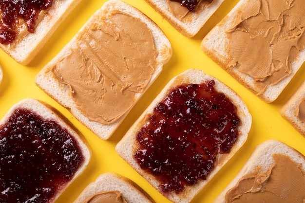 Photo full frame shot of bread slices with peanut butter and preserves arranged on yellow background