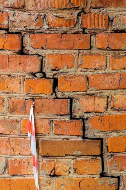 Foto fotografia completa di un muro di mattoni con una crepa diagonale e un nastro di avvertimento a strisce bianche e rosse