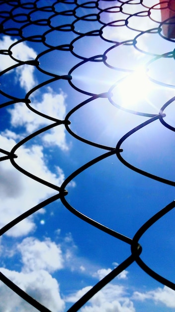 Full frame shot of chainlink fence against blue sky on sunny day