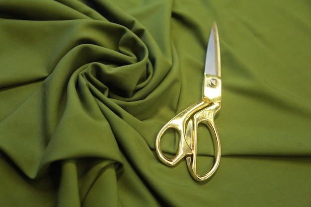 full frame shot of golden metal scissors on a folded green fabric