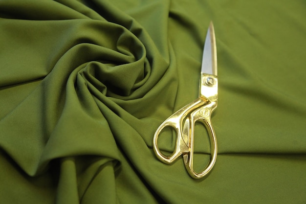 Photo full frame shot of golden metal scissors on a folded green fabric