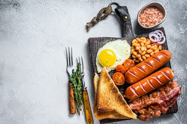 Full fry up Engels ontbijt met gebakken eieren, worstjes, spek, bonen en toast op een houten snijplank.