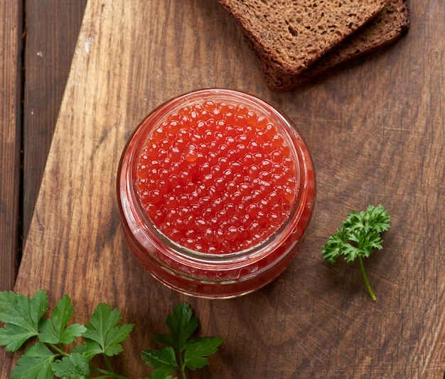 Full glass jar with red caviar on a brown wooden table top view