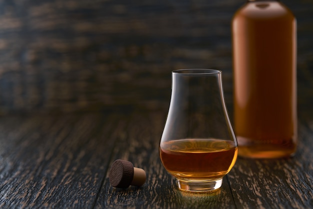 Full glass of whiskey and whisky bottle and cork  on a wooden table,