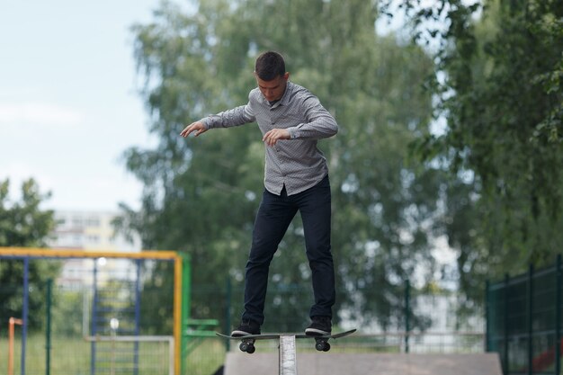 Full growth shot - cute young brunette skateboarder shows trick with skateboard in summer sunny park