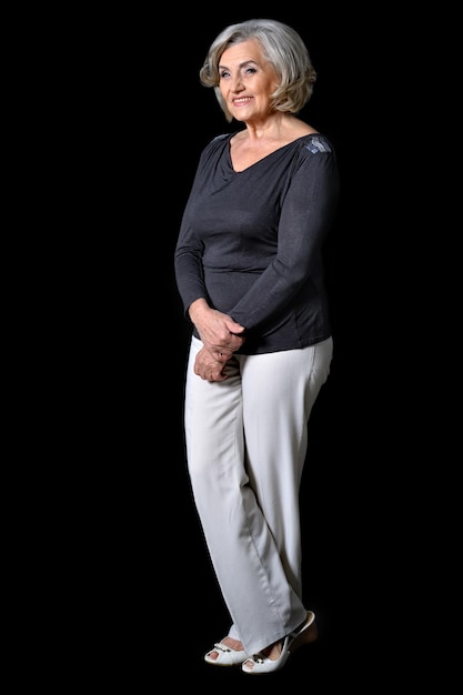 Full height portrait of mature woman posing against black background