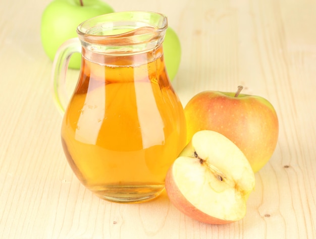 full jug of apple juice and apple on wooden background