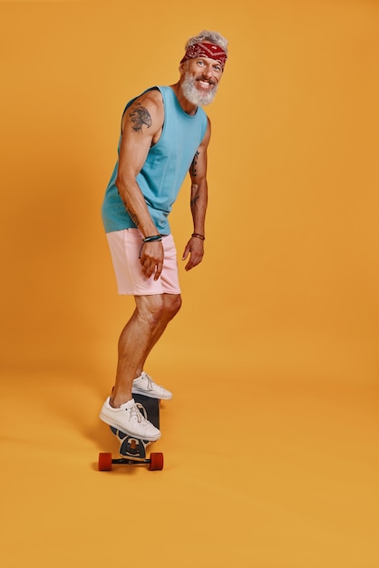 full length of active senior man skateboarding against orange background