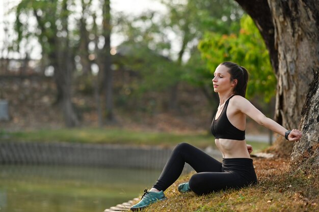 美しい日光のある公園でのトレーニングセッション後に休む運動女性の全長健康的なライフスタイルのコンセプト