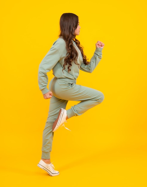 Full length of attractive cheerful girl in sport wear isolated over yellow background Sportwear for teenager child