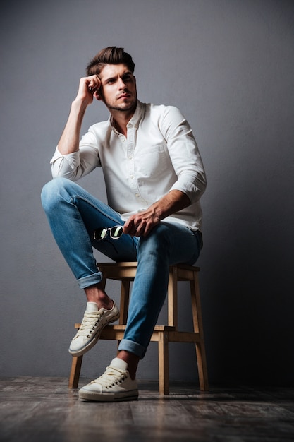 Full length of attractive young man in white shirt and jeans holding sunglasses