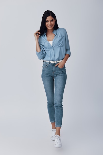 Full length of attractive young woman  and smiling while standing against grey wall