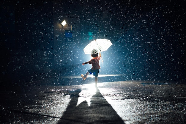 雨の中で傘を握っている赤ちゃんの女の子の全長