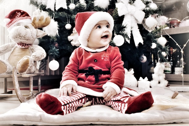 Photo full length of baby girl wearing santa hat by christmas tree