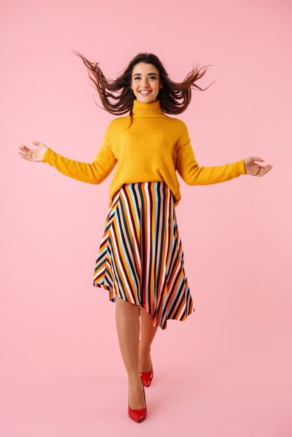 Full length of a beautiful young woman wearing colorful clothes standing isolated over pink, posing