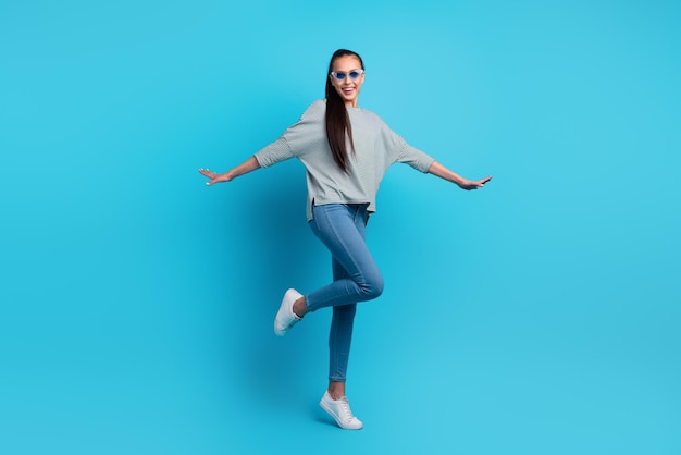 Full length body size photo of pretty cheerful carefree girl having fun dancing isolated over blue color background