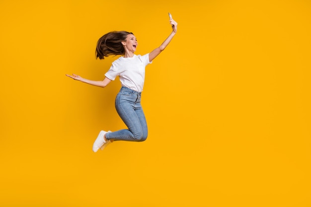 Full length body size photo of woman taking selfie throwing\
hair jumping smiling isolated on bright yellow color background\
with copyspace