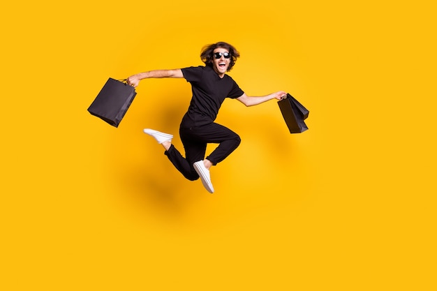 Full length body size portrait of man jumping up keeping packages after sale on black friday isolated on bright yellow color background