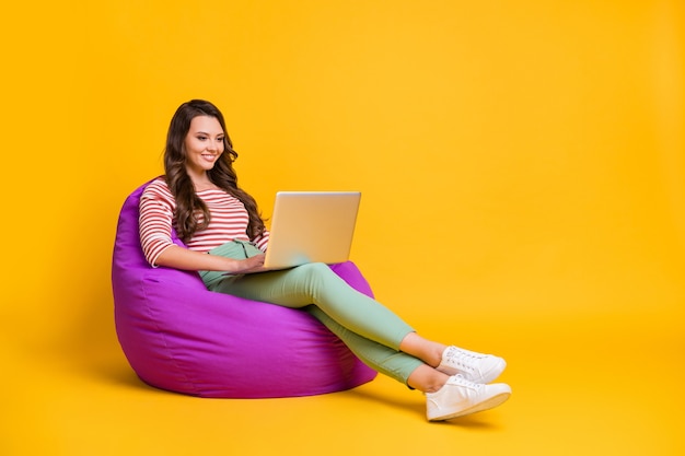 Full length body size side profile photo girl sitting in soft chair working with laptop smiling isolated on bright yellow color background