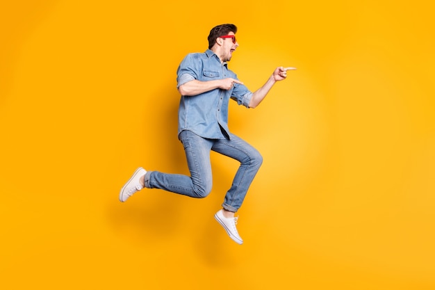 Full length body size view of nice attractive funky crazy cheerful cheery guy jumping pointing aside advert hot tour trip isolated over bright vivid shine vibrant yellow color wall