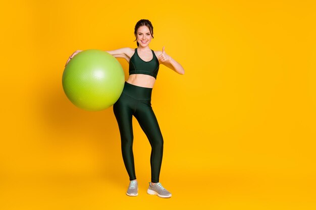 Full length body size view of nice sportive cheerful girl carrying fitness ball showing thumbup isol