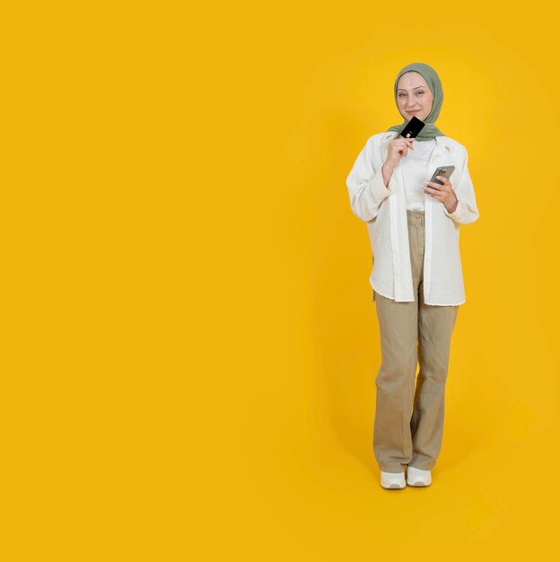 Full length body view young dreamy thoughtful muslim girl in hijab holding credit card copy space