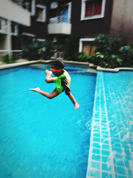 Photo full length of boy diving into swimming pool against building