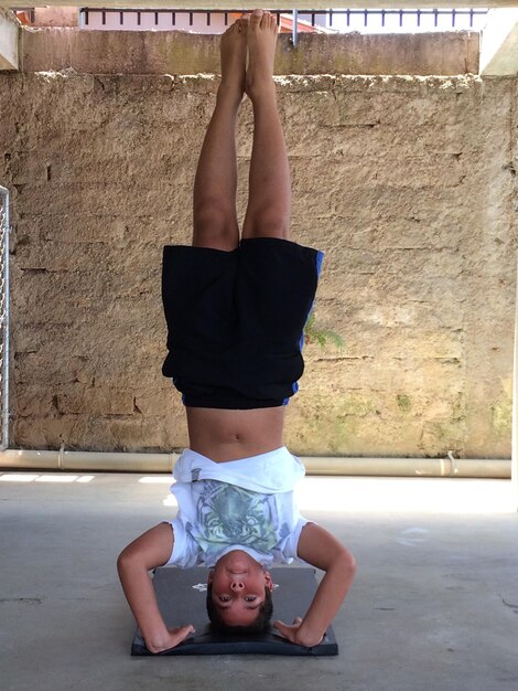 Photo full length of boy doing headstand against wall