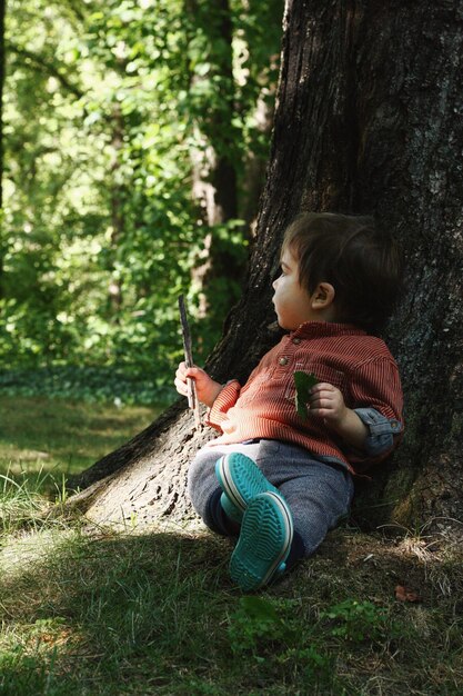 公園の木のそばでリラックスしている男の子の長さ