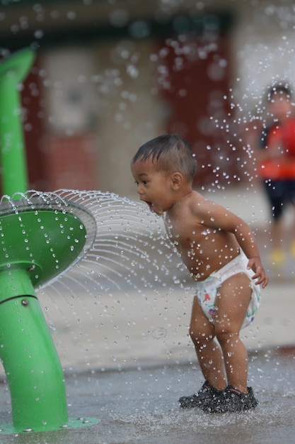 水の噴水のそばに立っている男の子の全長