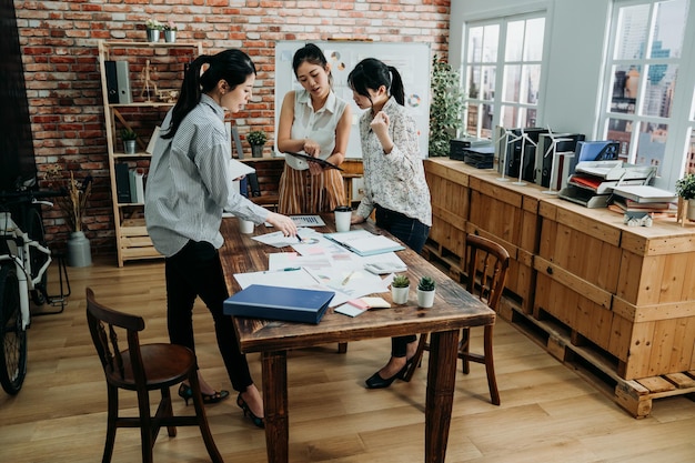 full length of business colleagues meeting in modern room with city view through window. three busy ladies coworkers discussing new plan for company sales in office. wooden vintage style workplace.